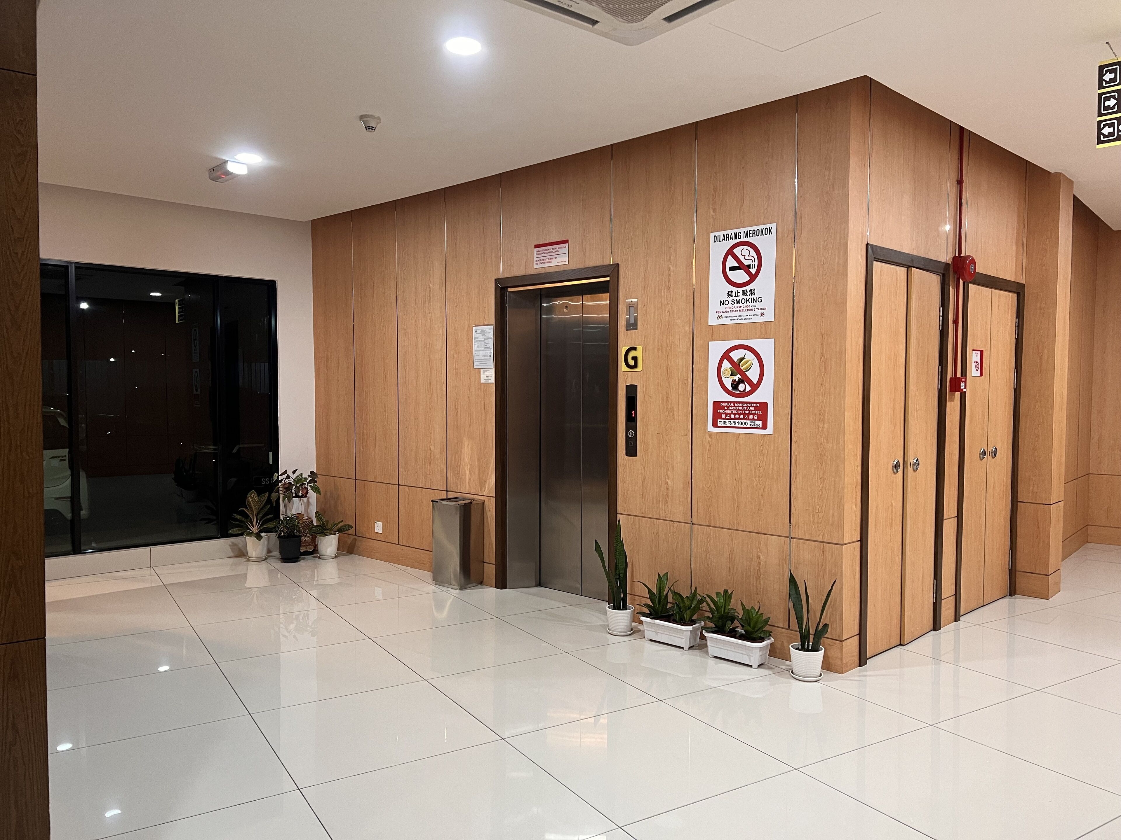 A clean, modern lobby with a wooden reception desk, a glass door entrance, and a sign indicating a smoking and no food policy.