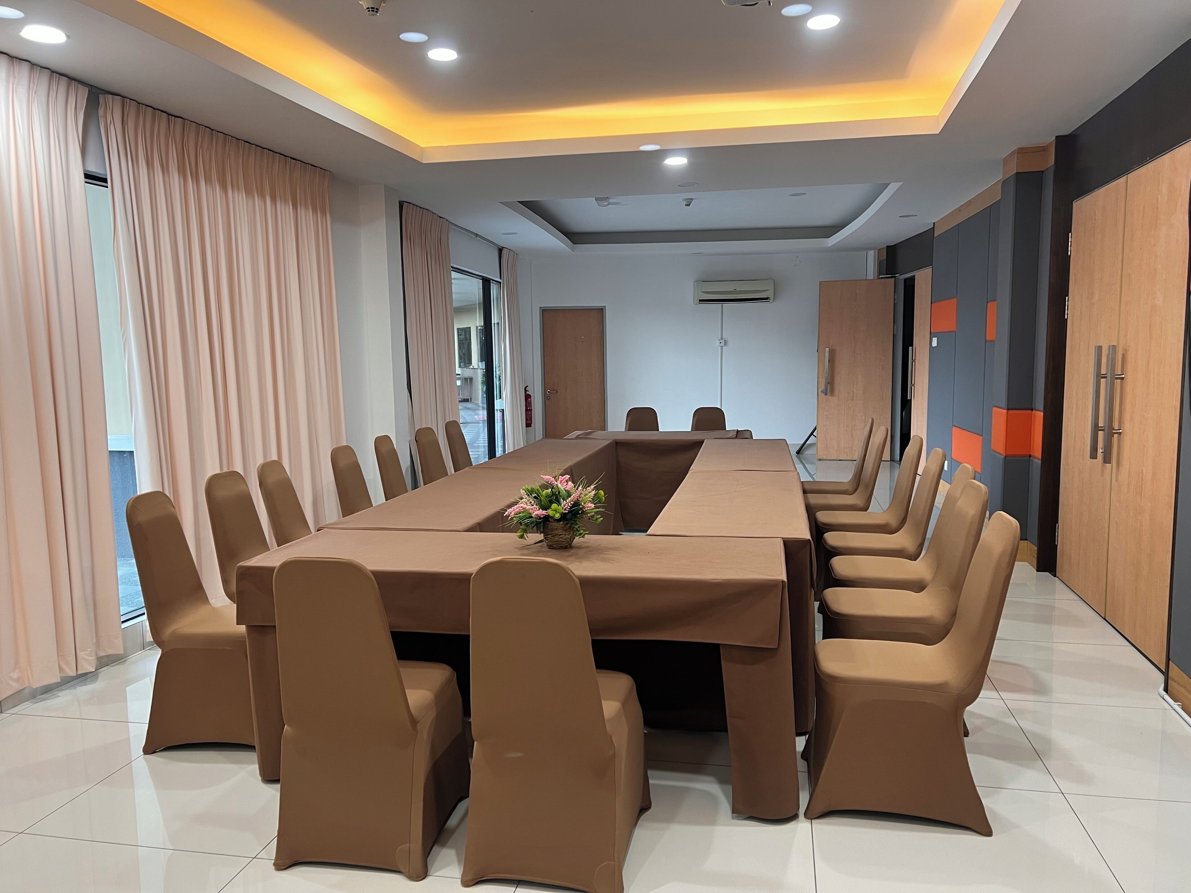 Un salón de conferencias con una larga mesa, sillas marrones y un centro de mesa con flores.