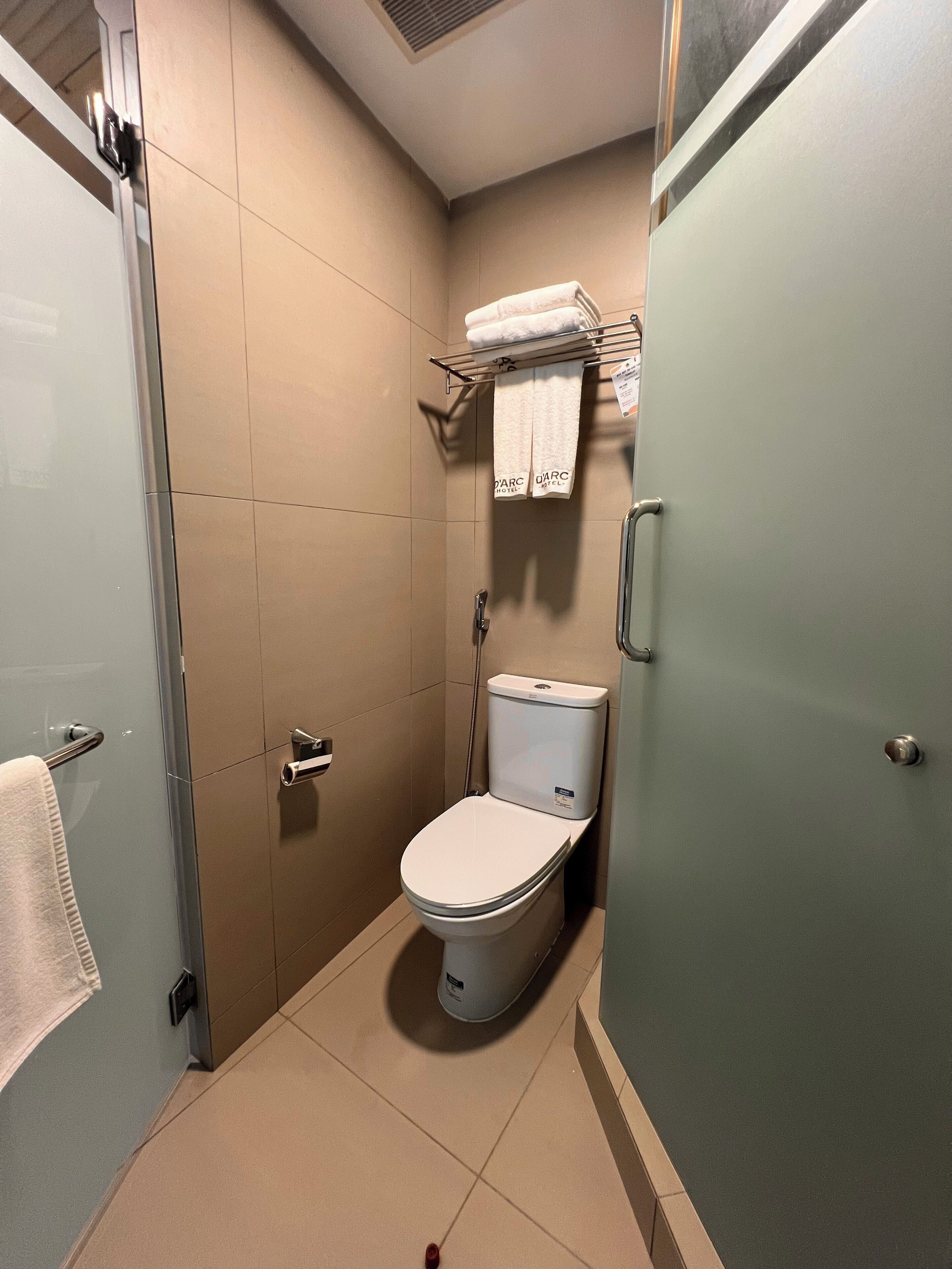 A compact bathroom with a toilet, a shower, and a towel rack with towels.