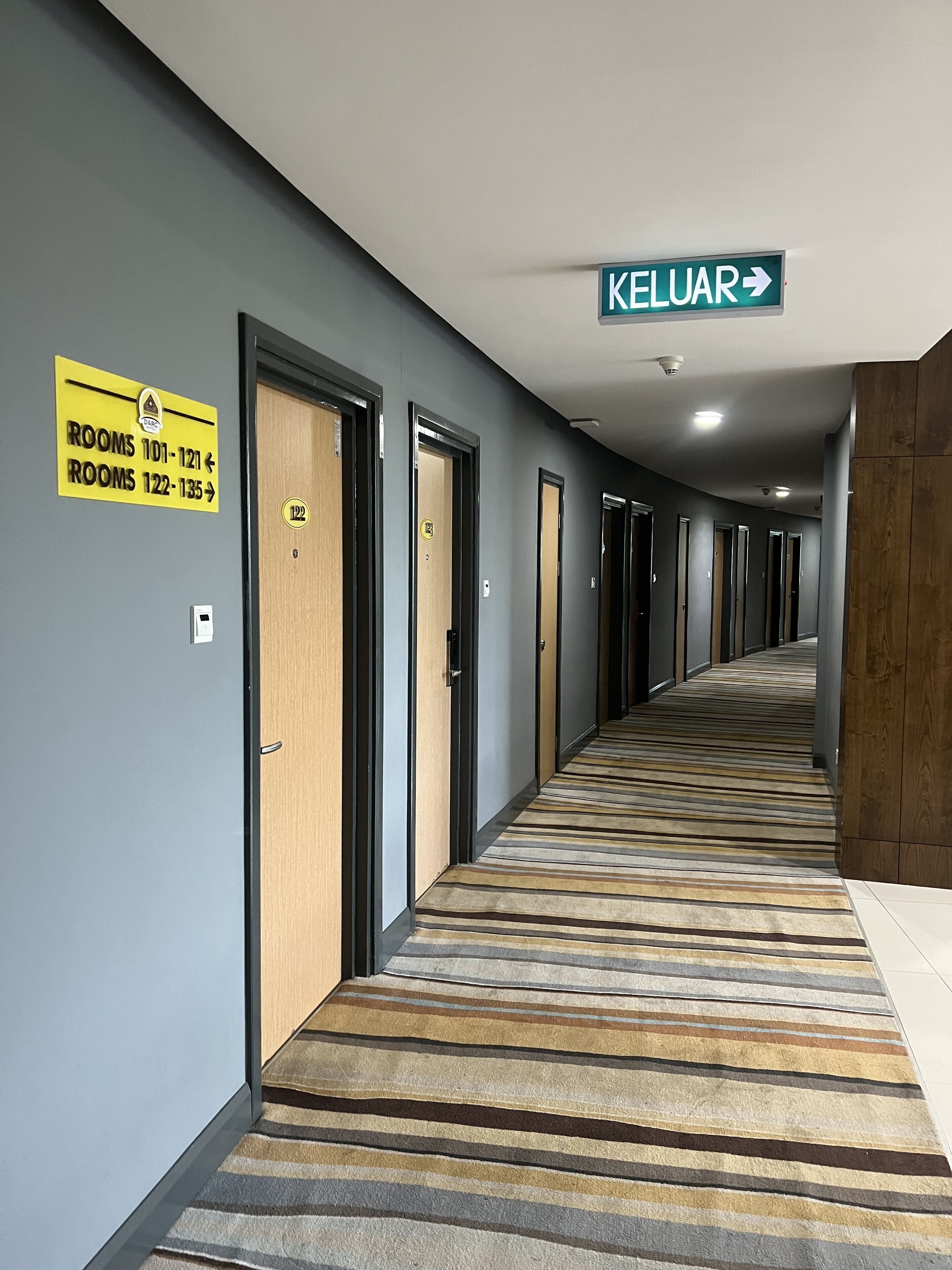Pasillo de hotel con puertas numeradas y un cartel que indica el camino a la cocina.
