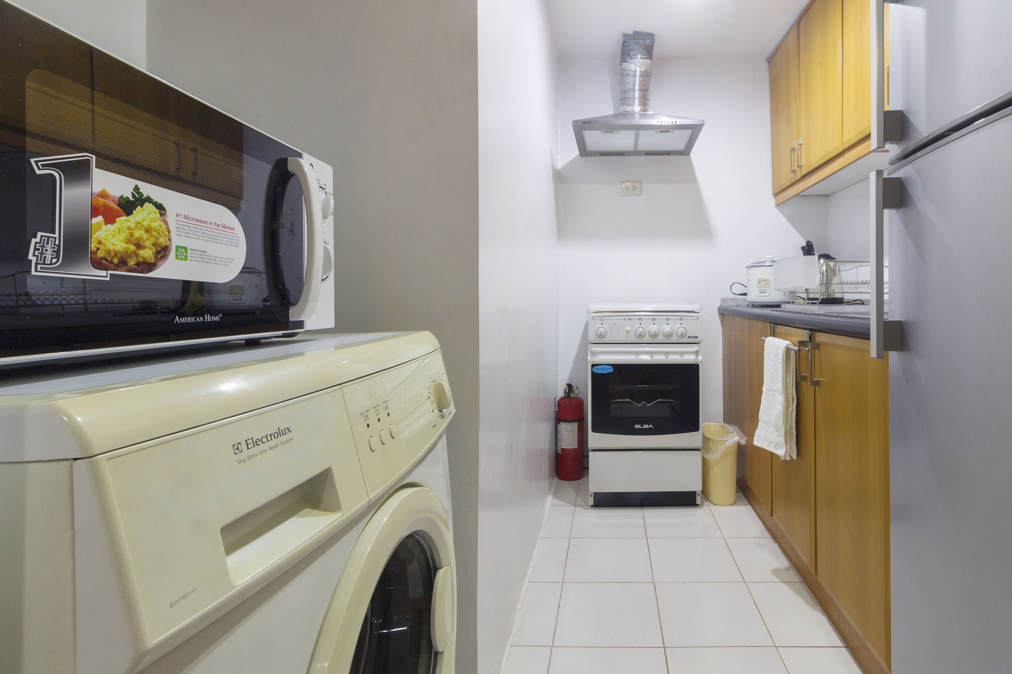 A compact kitchen with a washing machine, microwave, oven, and wooden cabinets.
