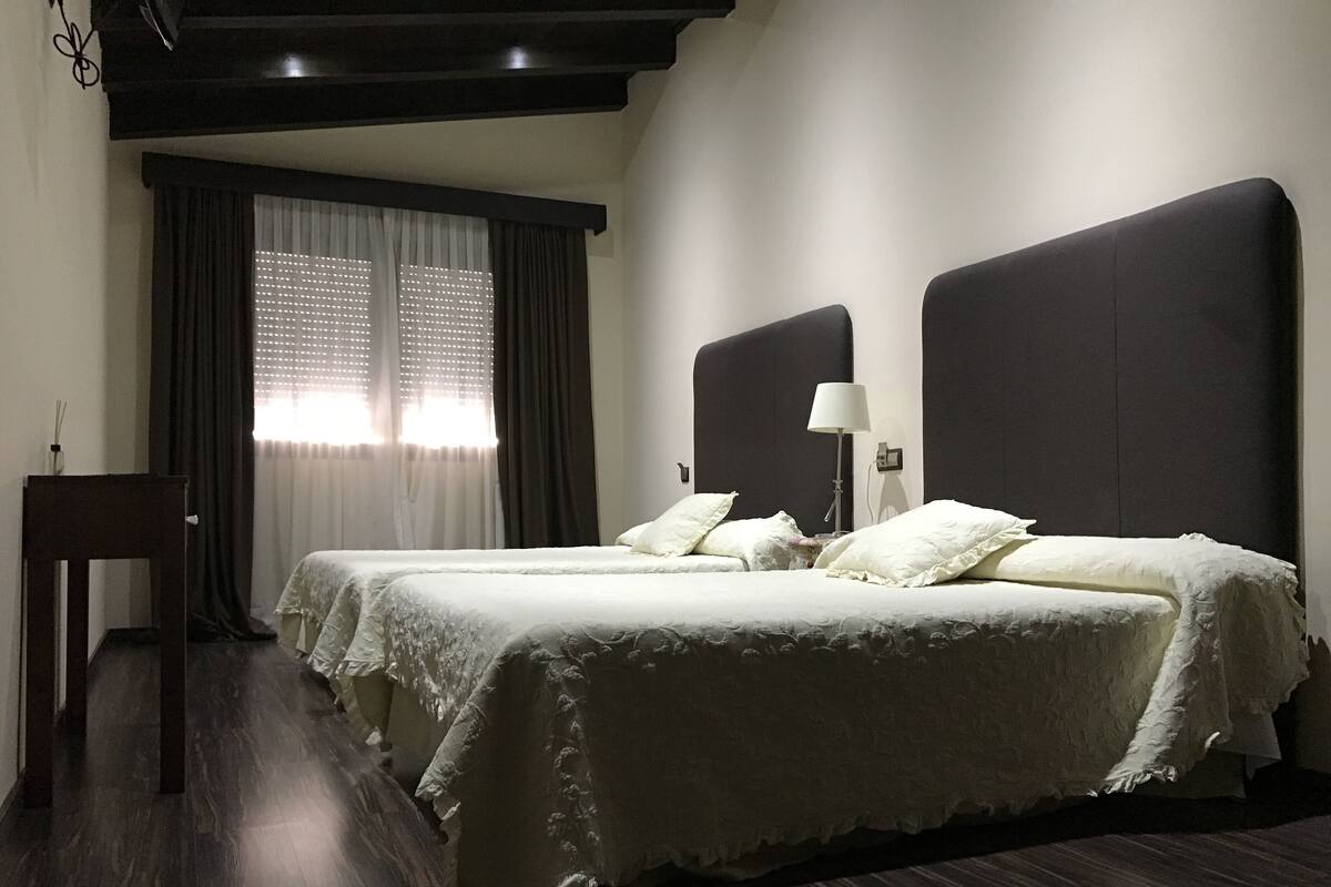 Habitación de hotel con dos camas, un escritorio, una lámpara y un ventanal con cortinas.