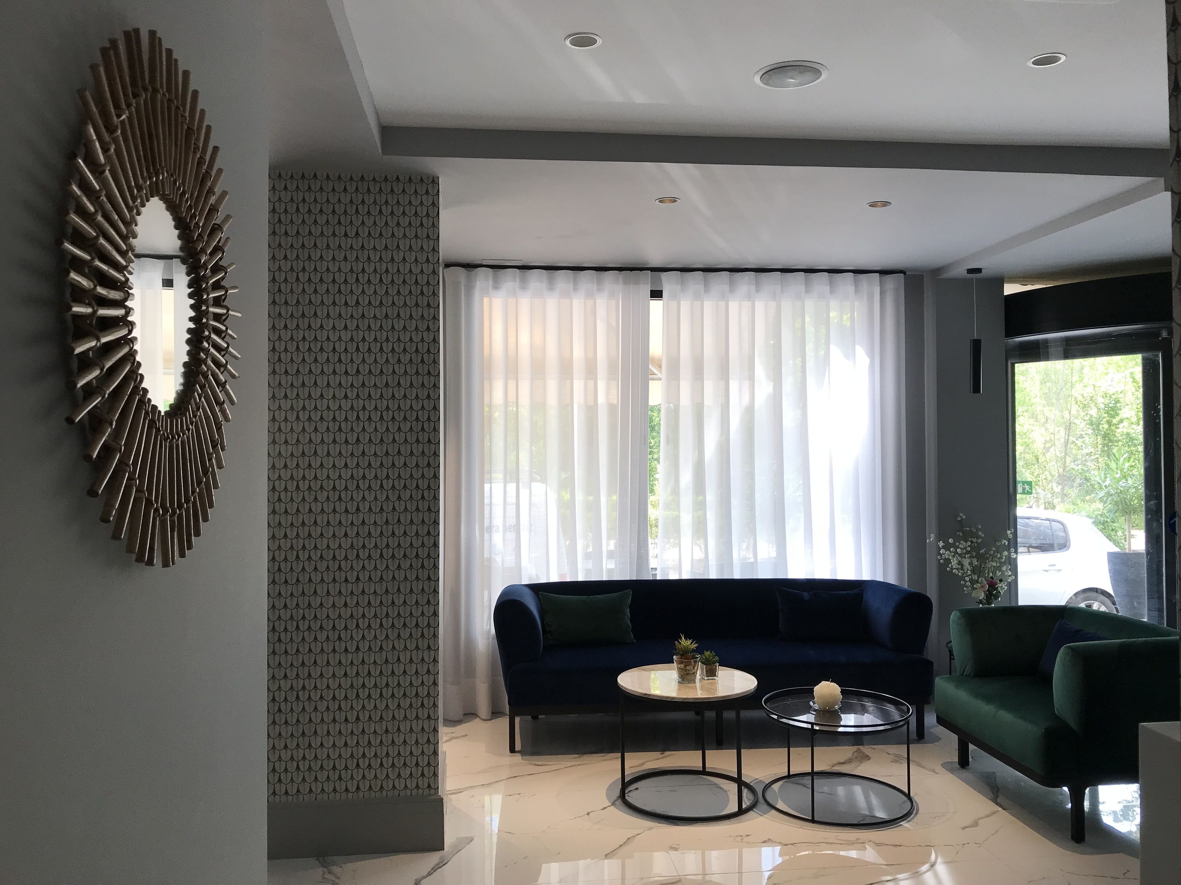 Una sala de estar moderna con un sofá azul oscuro, dos mesas redondas de centro y un espejo decorativo.