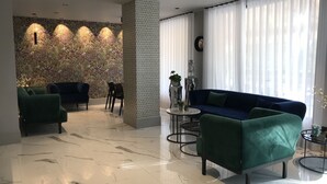 Een moderne woonkamer met een blauwe bank, groene fauteuils en een marmeren vloer.