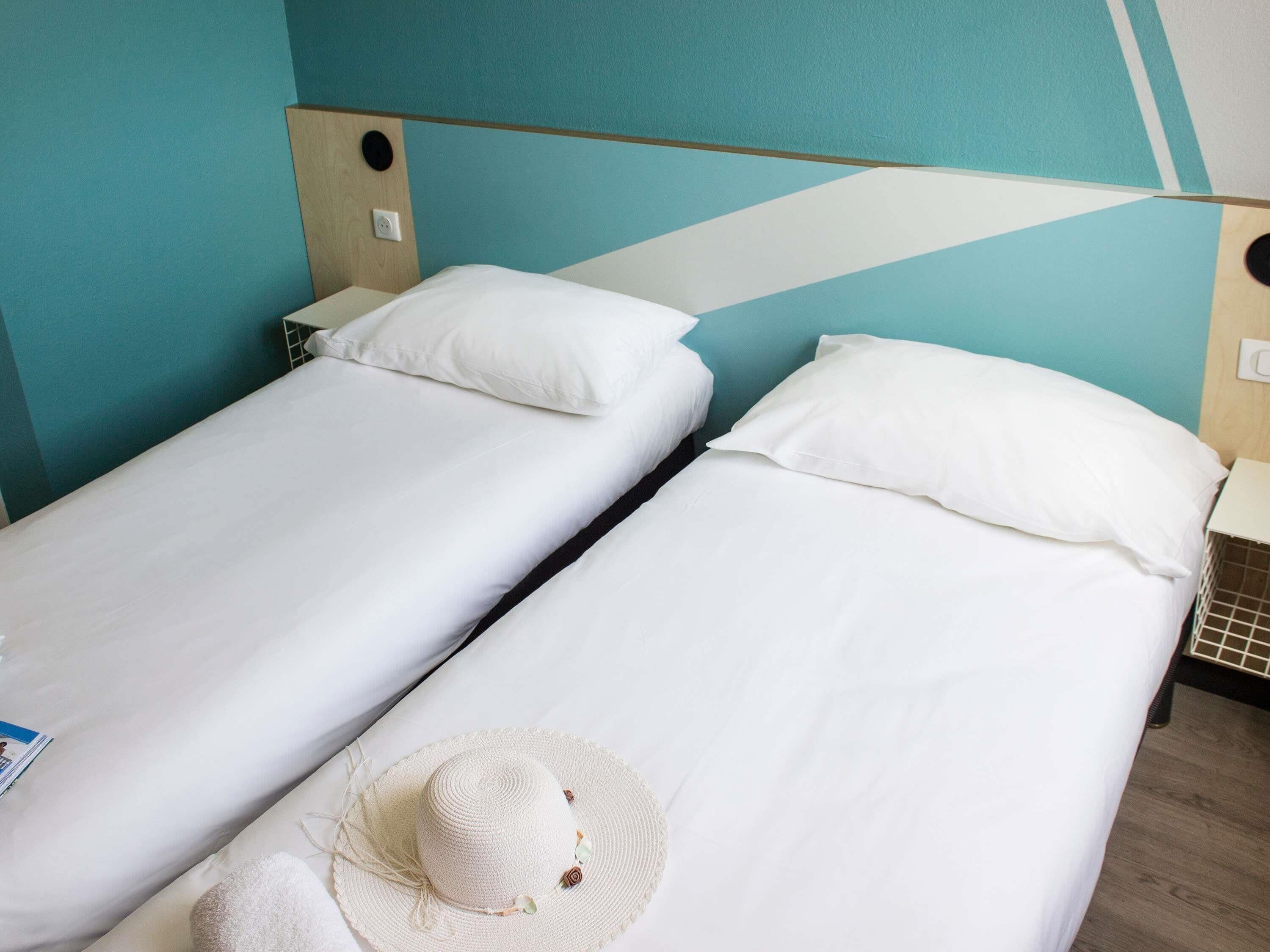 Two single beds with white linens in a room with teal walls and a wooden headboard.