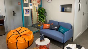 Een moderne kantoorruimte met een blauwe bank, een oranje relaxstoel en een klein tafeltje met een bord.