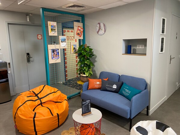 Een moderne kantoorruimte met een blauwe bank, een oranje relaxstoel en een klein tafeltje met een bord.