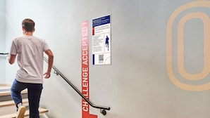 Een persoon daalt een trap af met een bord in rood en wit waarop staat 'CHALLENGE ACCEPTED!' en een QR-code.