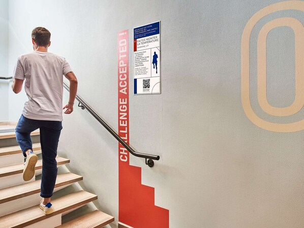Een persoon daalt een trap af met een bord in rood en wit waarop staat 'CHALLENGE ACCEPTED!' en een QR-code.