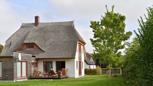 Een huis met rieten dak, een houten terras en een verzorgd gazon.