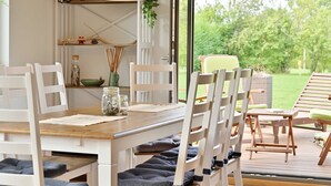 Een eetruimte met een houten tafel, witte stoelen en uitzicht op de omgeving.