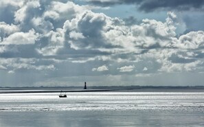 A beach with a boat and a lighthouse in the distance.