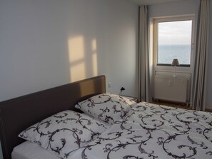 A bedroom with a bed, a window with curtains, a radiator, and a lamp on a bedside table.