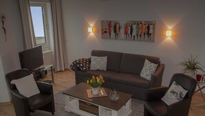 Una sala de estar con un sofá, dos sillones, una mesa de centro con un jarrón de flores y un cuadro en la pared.