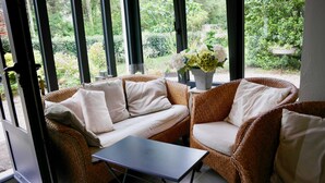 A wicker sofa with white cushions and a small table in a room with large windows. - 700m from Plage des Dames - House for 9 (Noirmoutier-en-l´Ile)