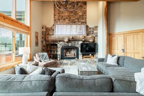 A cozy living room with a stone fireplace, a television, and a large window.