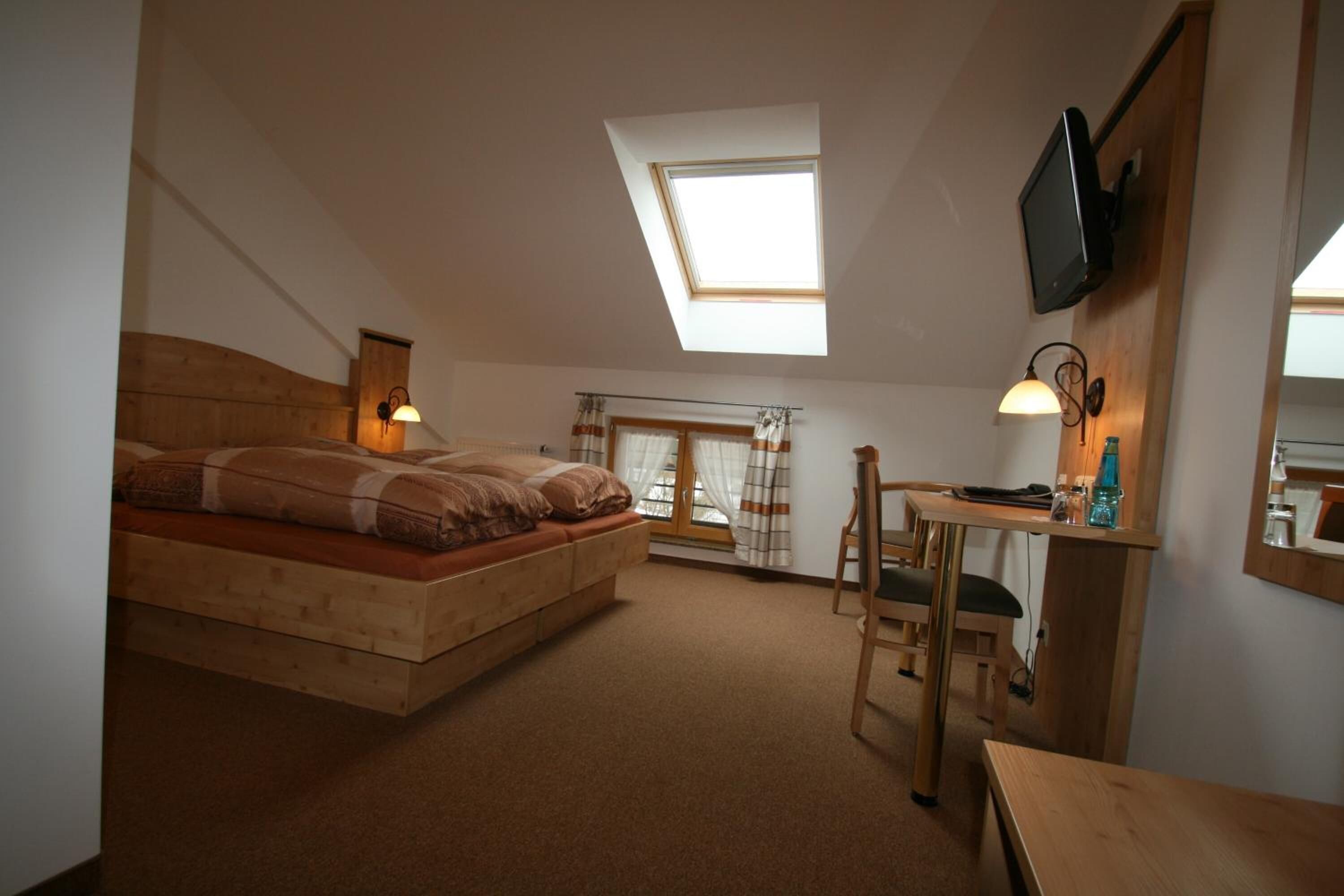 A bedroom with a loft bed, skylight, TV, desk, and chair.