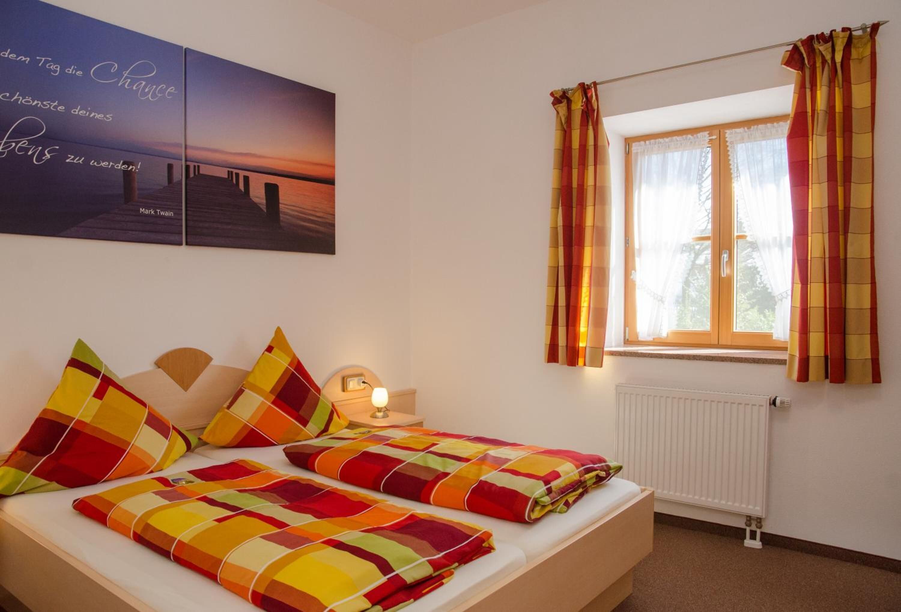 A bedroom with two beds, a window with curtains, a radiator, and a wall with a sunset painting.