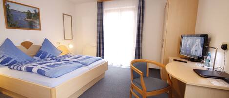 A hotel room with a bed, a desk with a computer, a chair, a TV, and a window with curtains.