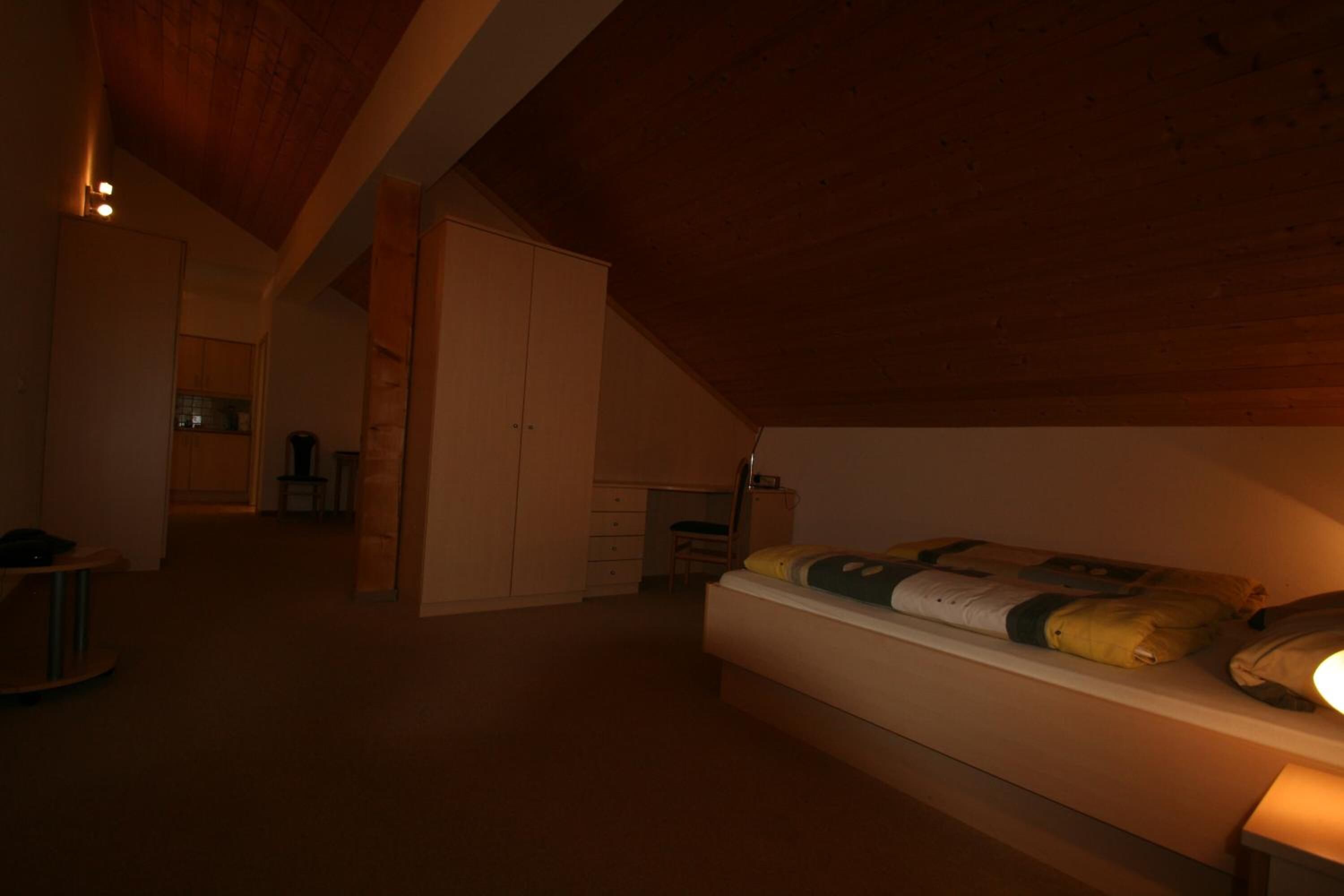 A bedroom with a sloped ceiling, a bed with pillows, a desk, and a chair.