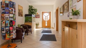 Un vestíbulo de hotel con una recepción, una vitrina con folletos, una planta en maceta, un acuario y una puerta con un diseño geométrico.