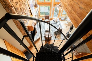 A spiral staircase leading to a living area with a stone wall, wooden flooring, and a view of the outdoors.