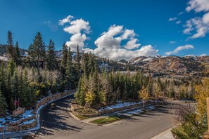 Un área de estacionamiento con una carretera curva, rodeada de árboles y parches de nieve, que conduce hacia un paisaje montañoso.