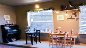 A cozy room with a piano, dining table, chairs, and a window with a view. - Harbour Inn guesthouse (Vesturbyggð)