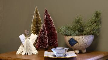 Una mesa de madera con adornos, incluyendo dos árboles de Navidad, un cuenco con ramas de pino y una jarra de cristal transparente.