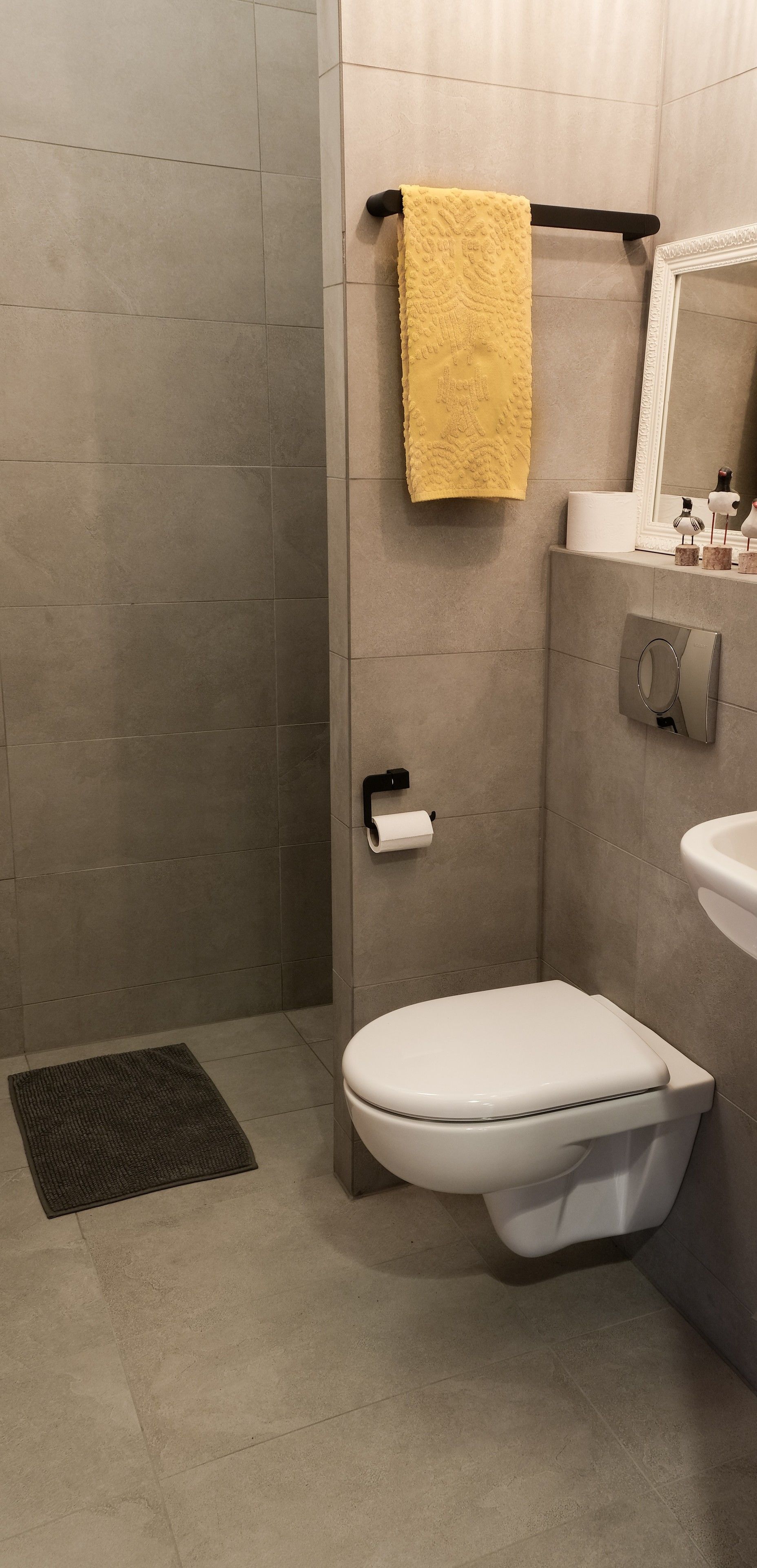 A modern bathroom with a toilet, a towel rack with a yellow towel, a toilet paper holder, and a mirror.