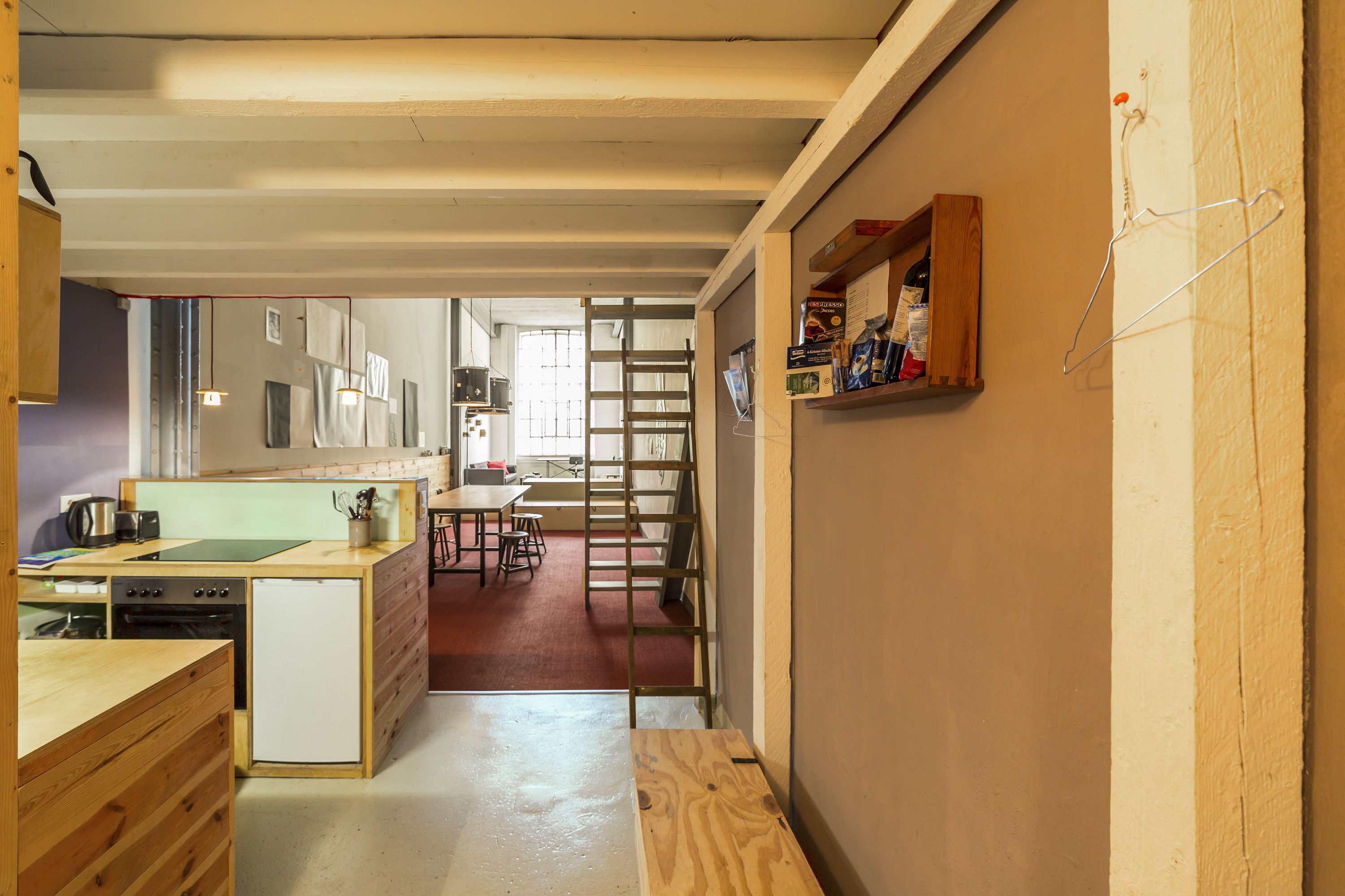 A compact kitchen with a dishwasher, a small refrigerator, and a wooden counter. There is a dining area with a table and chairs, and a ladder leaning against the wall.