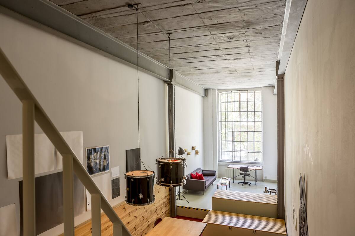 A spacious room with a high ceiling, a staircase, and a large window providing natural light.