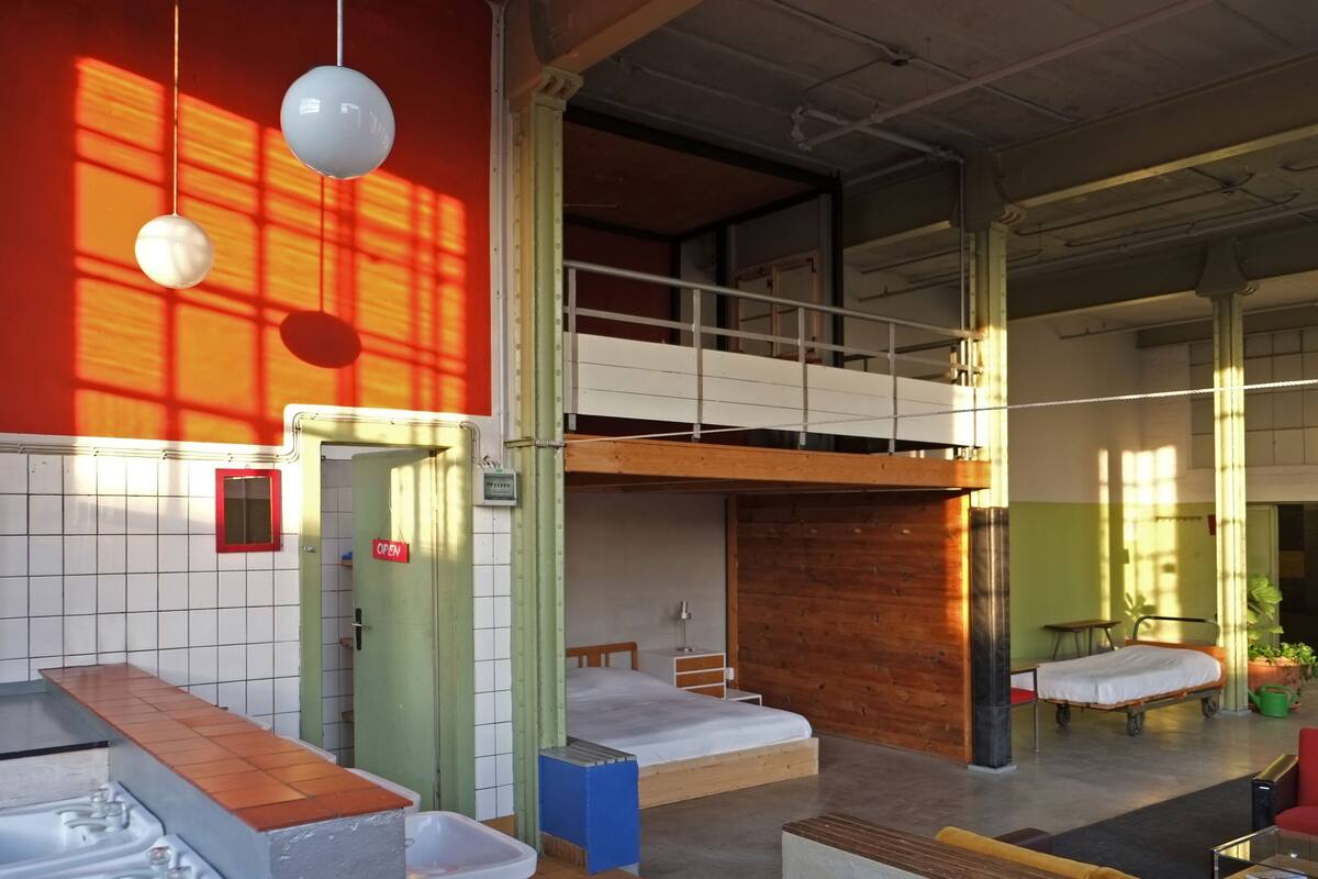 A dormitory room with bunk beds, a small desk, a chair, and a window with a view of the outside.