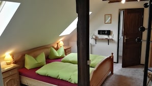 A bedroom with a sloped ceiling, a bed with green pillows, a bedside table with a lamp, a mounted TV, and a door with a mirror. - Radler-Scheune Thüringen (Friedrichroda)