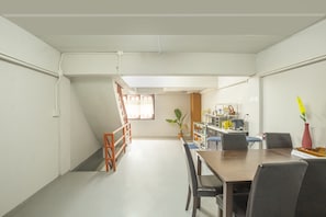 A spacious room with a dining table, chairs, a potted plant, and a kitchen area with cabinets and appliances. - OYO 723 Lamphun Hostel (Lamphun)