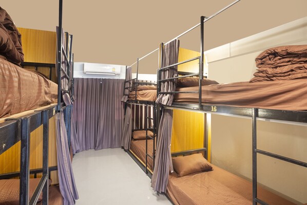 A dormitory room with bunk beds, a curtain, and an air conditioning unit.