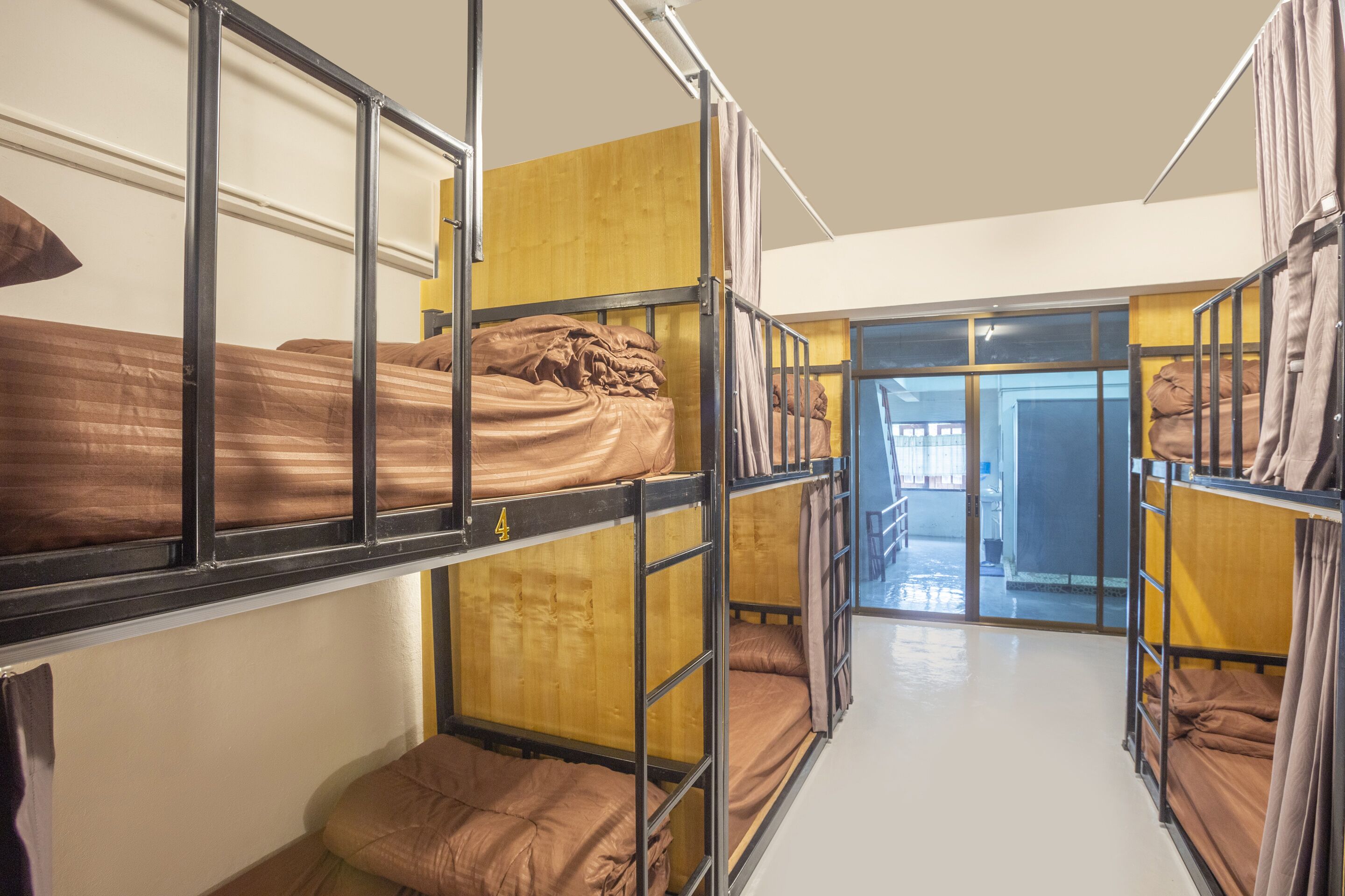 A bunk room with metal bunk beds, wooden panels, and a corridor leading to a bright area.