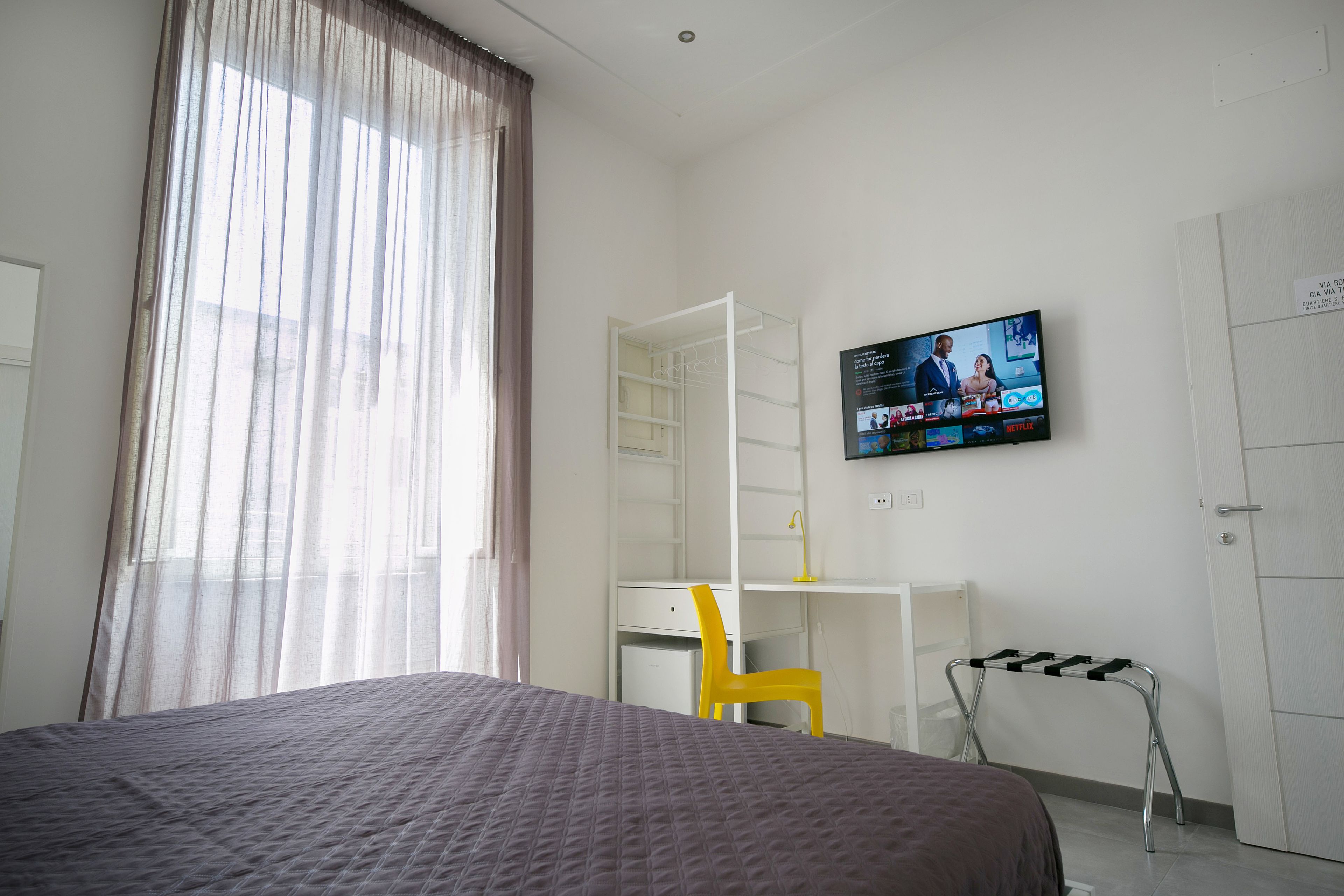 Ein Hotelzimmer mit Bett, Schreibtisch, Sessel und Fernseher an der Wand.