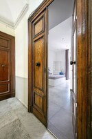 Een hal met een houten deur die leidt naar een slaapkamer met een bed, een dressoir en een stoel.