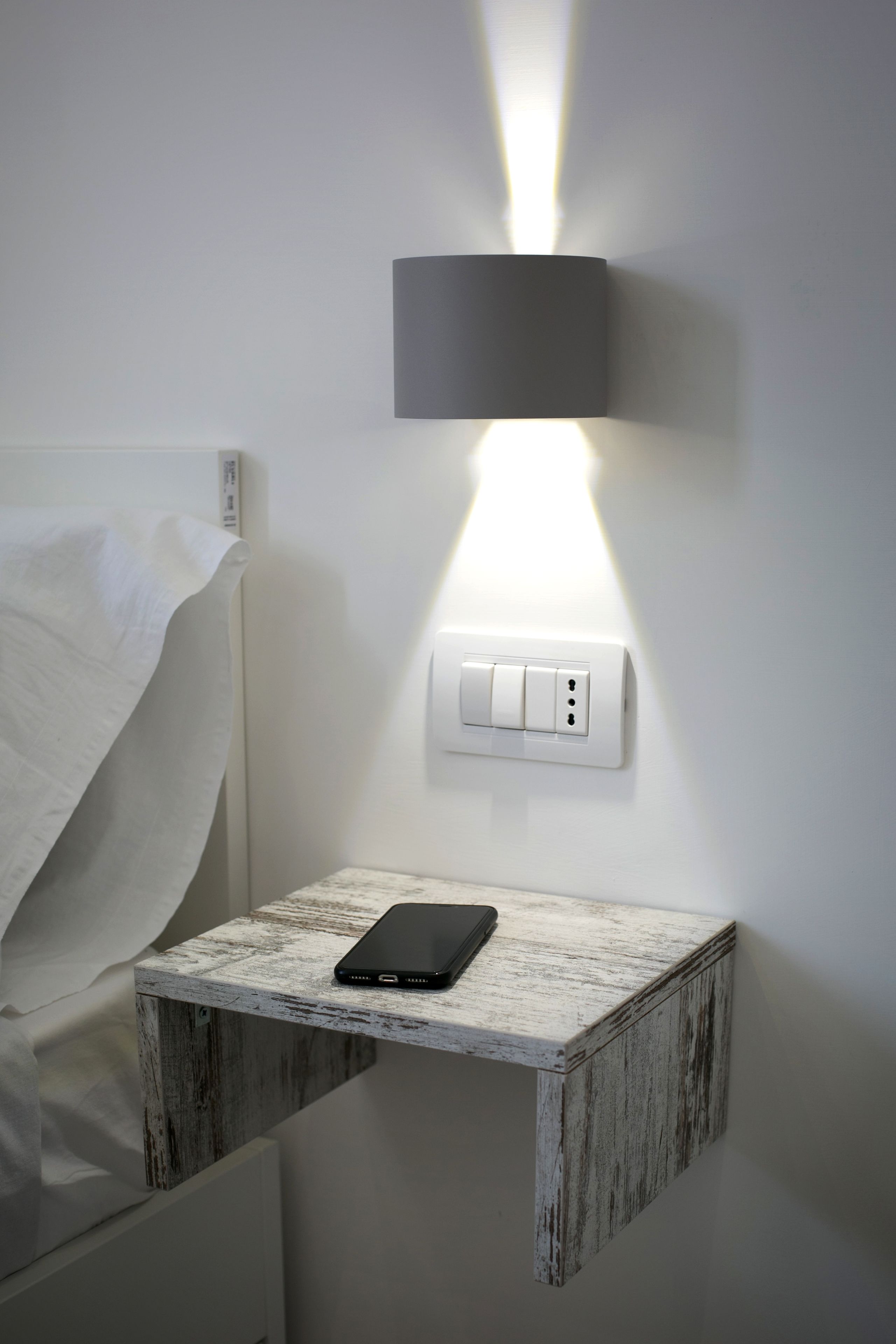 A bedside table with a tablet, a wall-mounted light, and a power outlet.