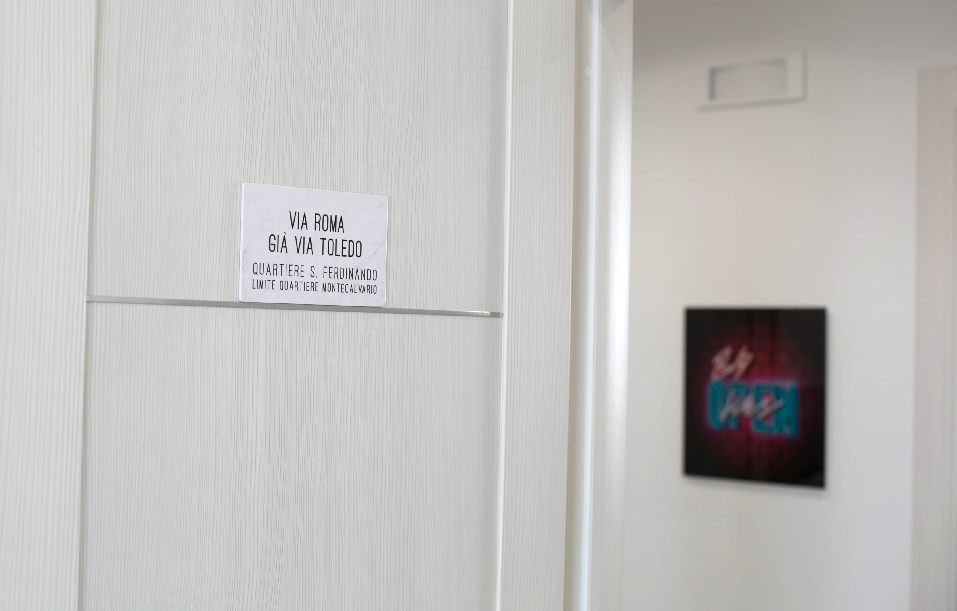 Una puerta blanca con un cartel que indica nombres de habitaciones y un letrero de neón al fondo.