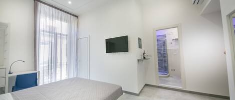 A modern hotel room with a bed, a desk, a chair, a TV, an air conditioning unit, and a shower area.