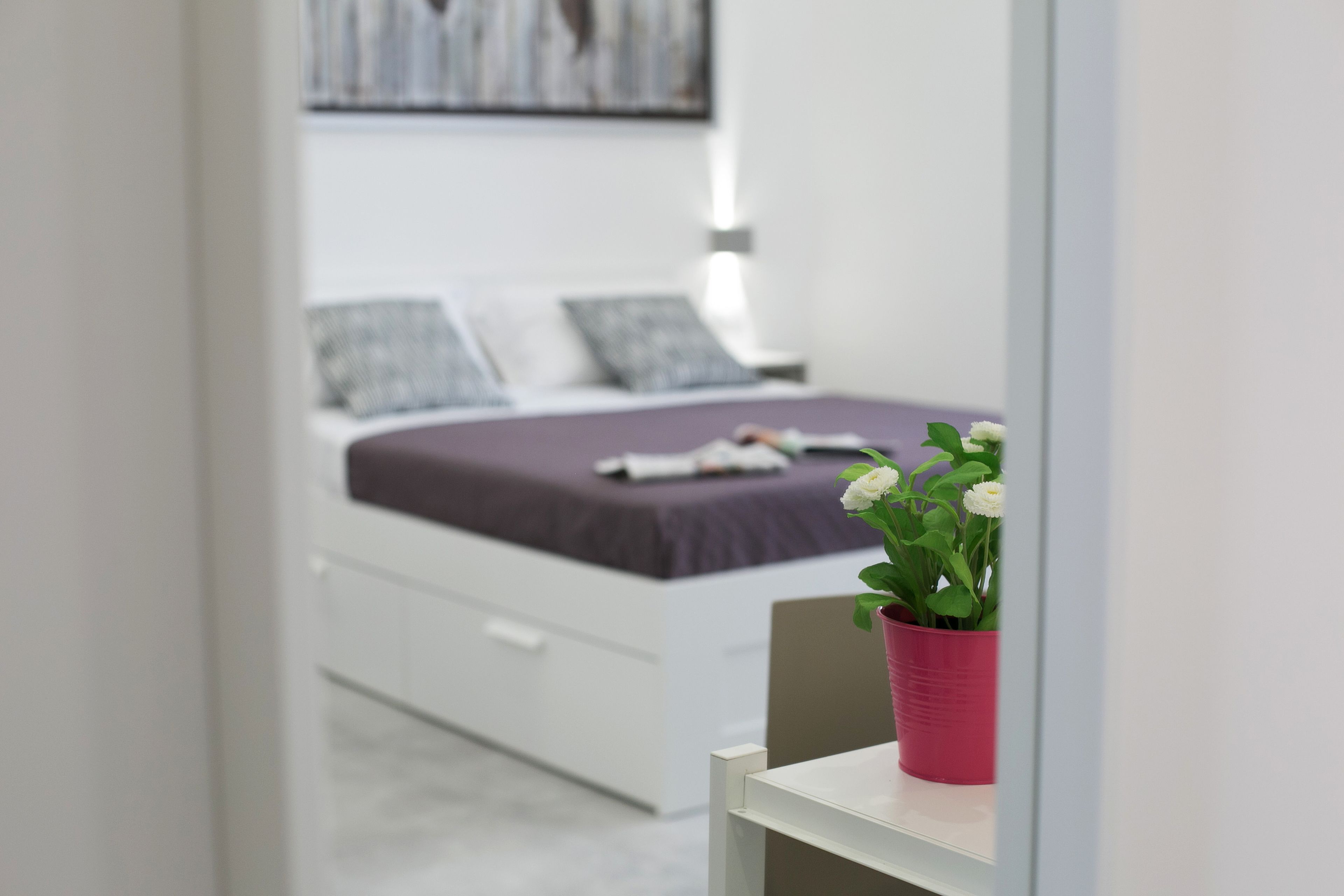 A bedroom with a bed, pillows, a nightstand, and a potted plant.