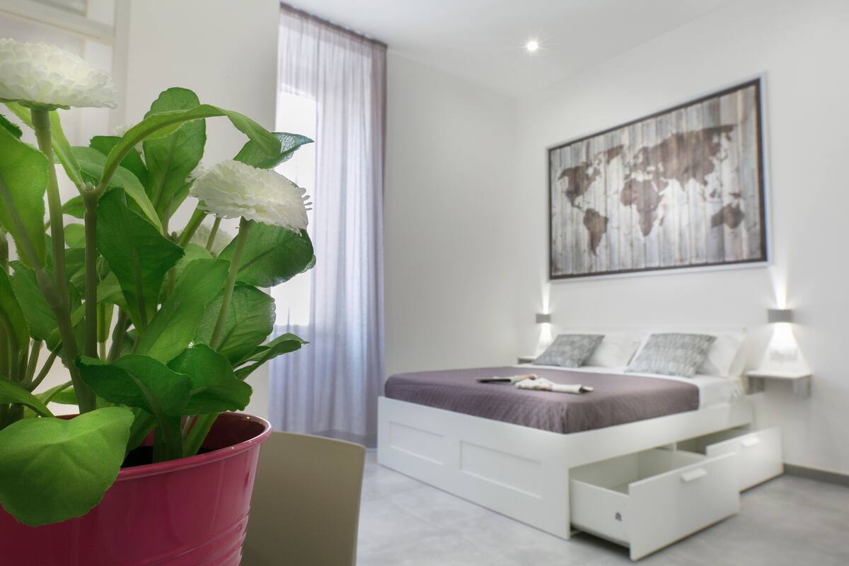 A modern bedroom with a bed, bedside tables, a world map artwork, and a potted plant.
