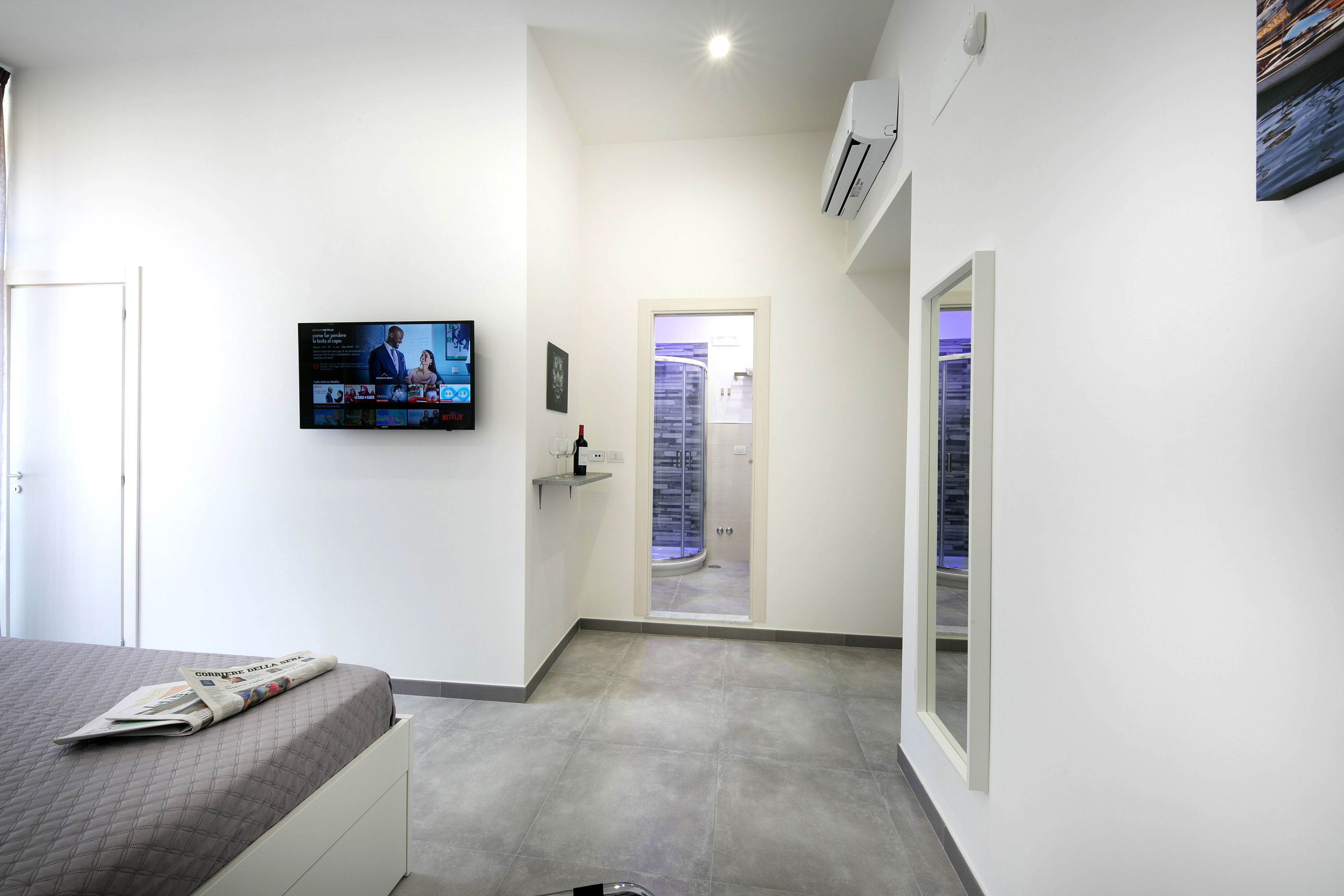 A modern hotel room with a bed, a television mounted on the wall, and a door leading to a bathroom.