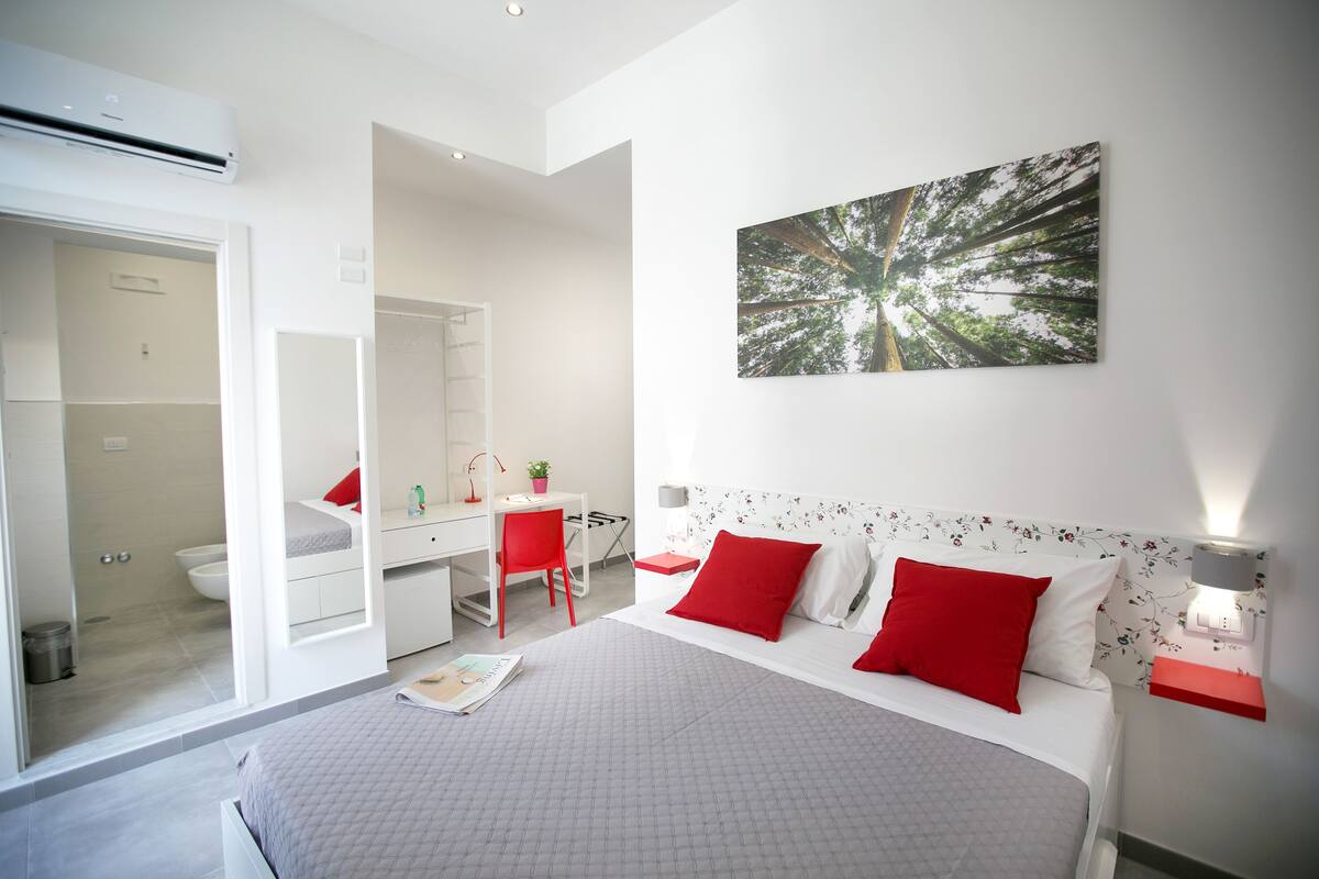 A modern bedroom with a large bed, a desk, and a shower area.