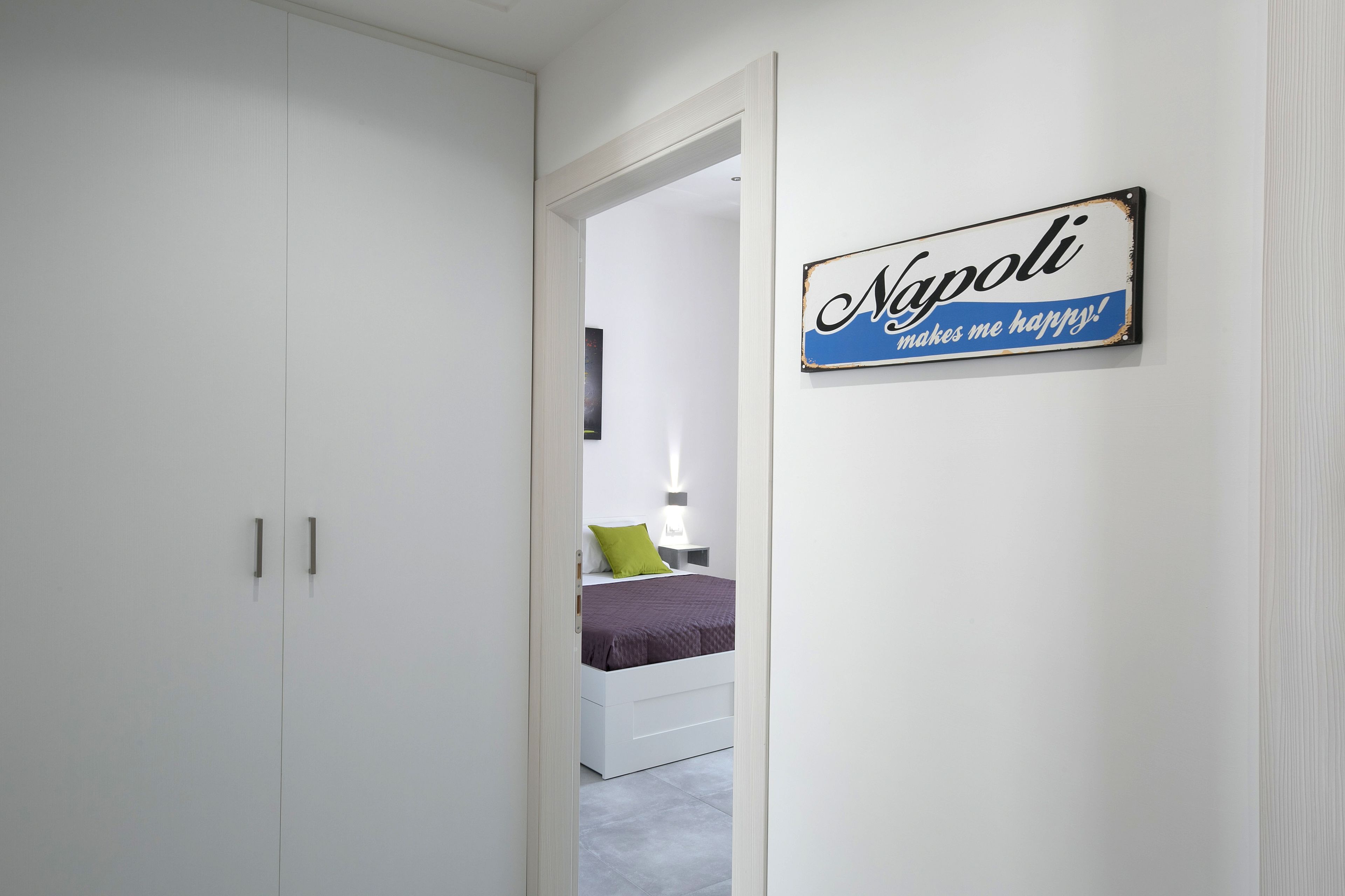 Un dormitorio con una cama, una mesita de noche y un cartel en la pared que dice 'Napoli me hace feliz'.