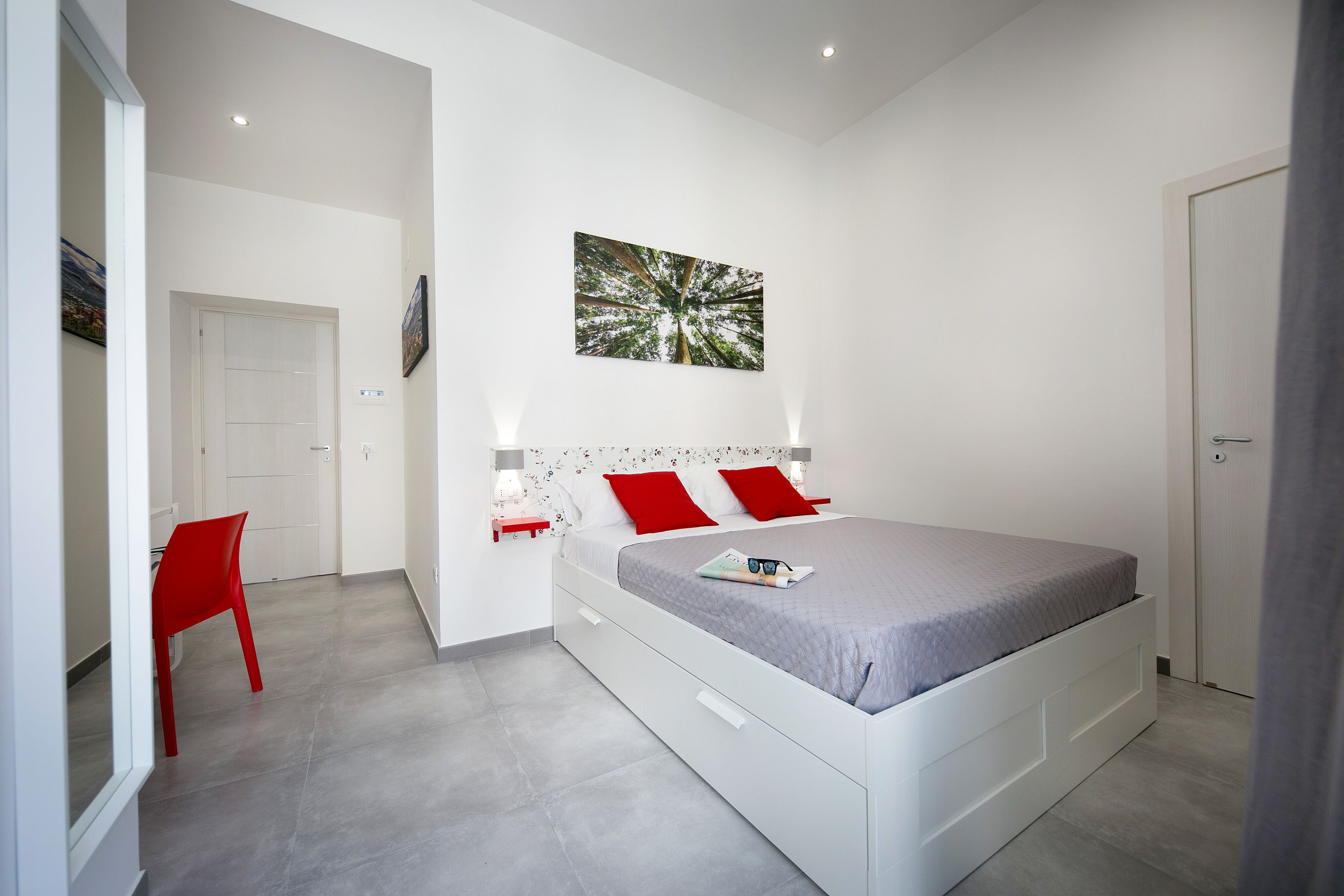 Una camera da letto moderna con un letto, una poltrona rossa e un quadro appeso al muro.