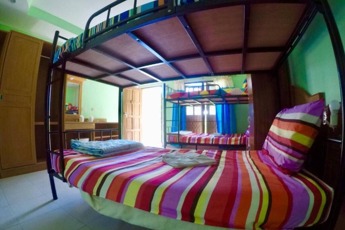 A bunk bed room with a striped bedspread, a wooden wardrobe, and a bathroom visible through an open door.