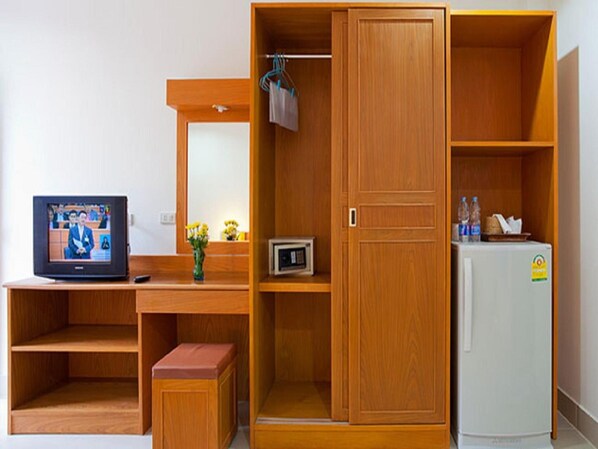 A compact room with a wooden wardrobe, a small desk with a television, a refrigerator, and a bench. - Grand View (Patong)